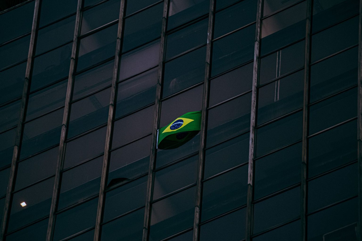 Bandeira do Brasil exposta na fachada de um edifício moderno de escritórios durante a noite