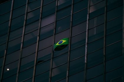 Bandeira do Brasil exposta na fachada de um edifício moderno de escritórios durante a noite