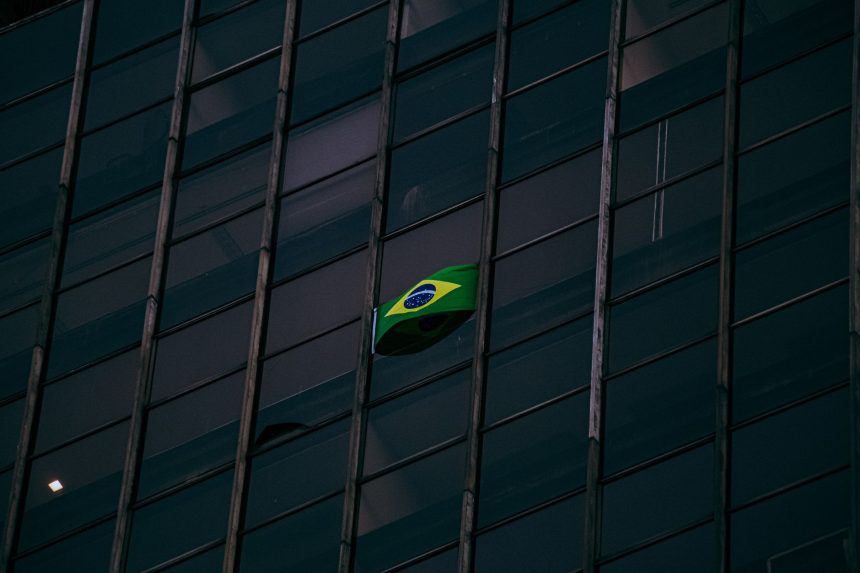 Bandeira do Brasil exposta na fachada de um edifício moderno de escritórios durante a noite